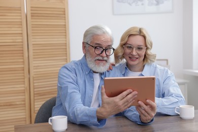 Photo of Senior man and mature woman watching something on tablet at home. Happy couple