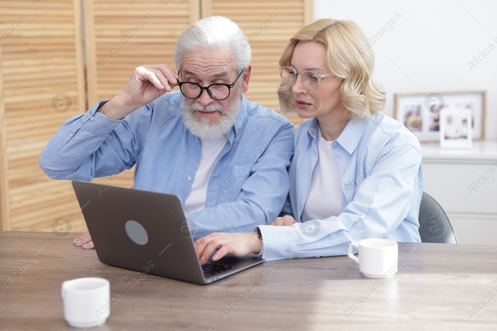 Photo of Senior man and mature woman watching something on laptop at home. Happy couple