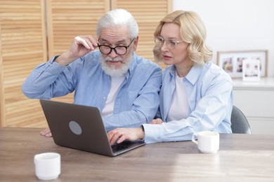 Photo of Senior man and mature woman watching something on laptop at home. Happy couple