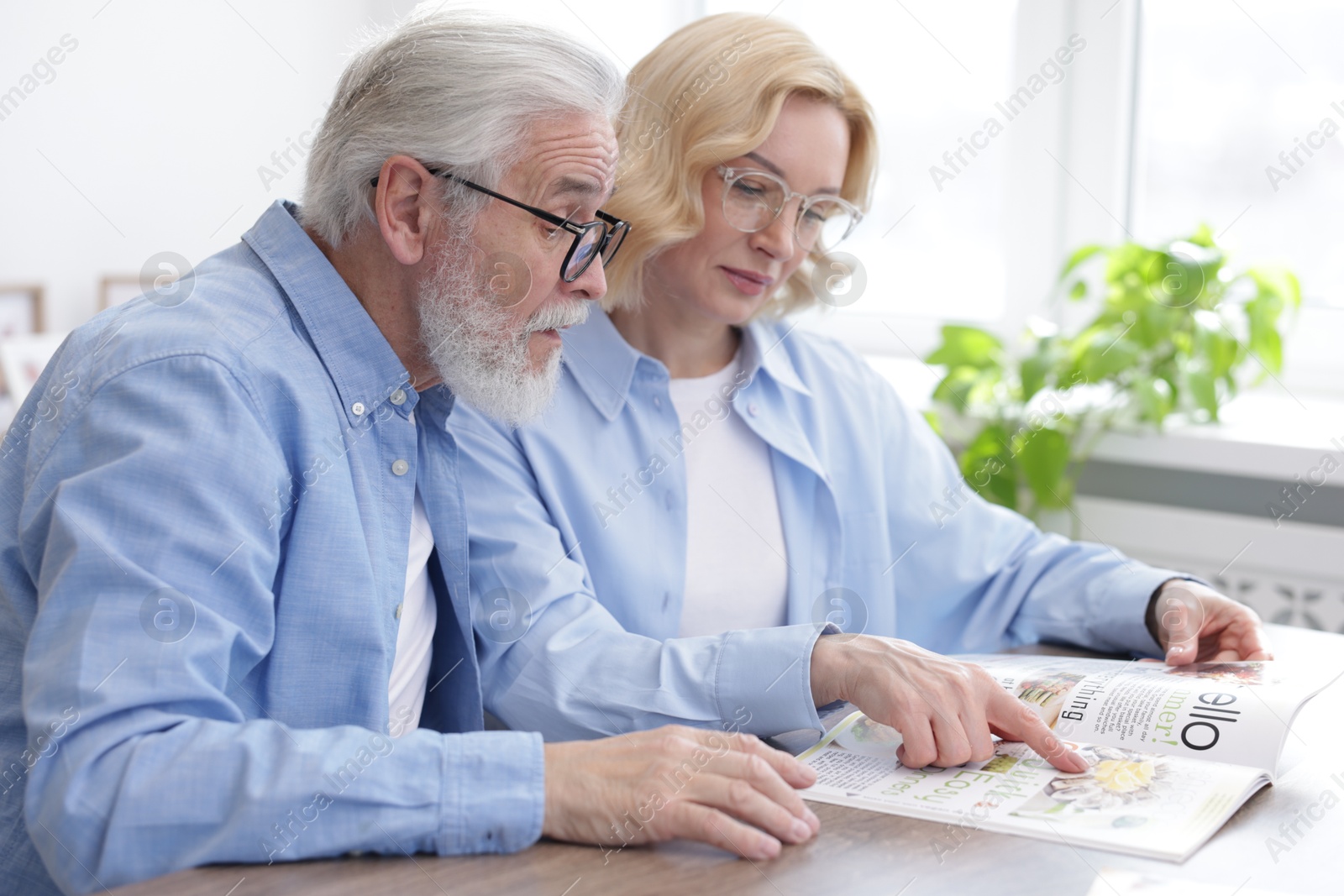 Photo of Senior man and mature woman reading magazine at home. Happy couple