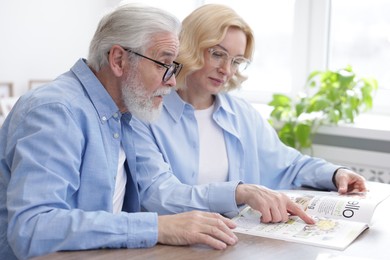 Photo of Senior man and mature woman reading magazine at home. Happy couple