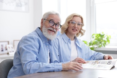 Senior man and mature woman reading magazine at home. Happy couple