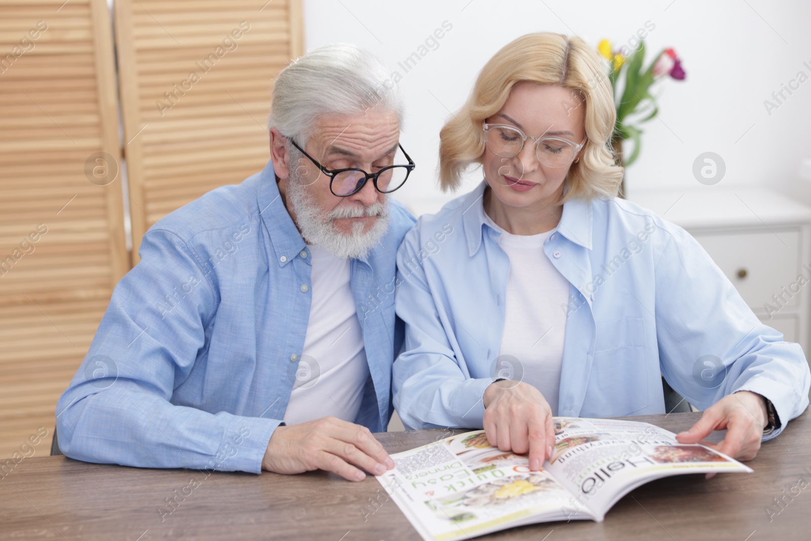 Photo of Senior man and mature woman reading magazine at home. Happy couple