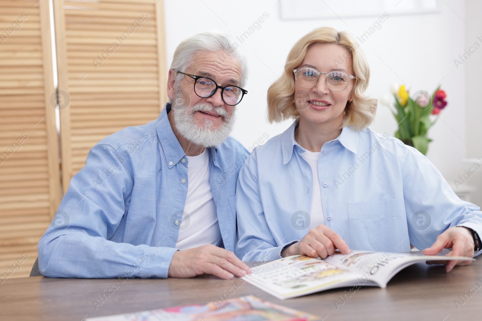 Photo of Senior man and mature woman reading magazine at home. Happy couple