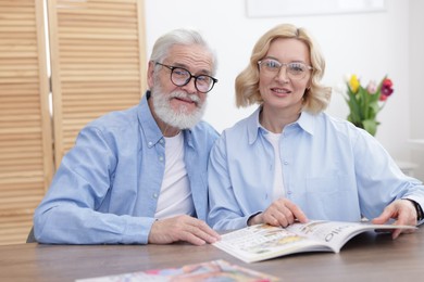 Photo of Senior man and mature woman reading magazine at home. Happy couple