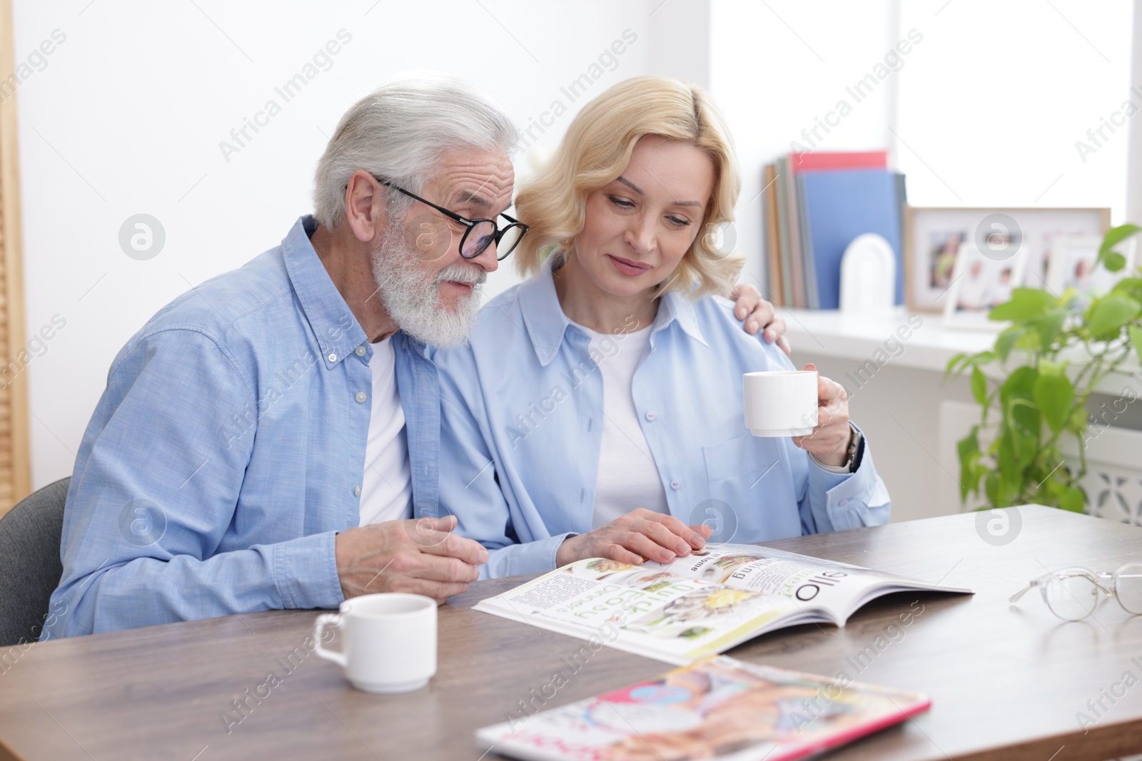 Photo of Senior man and mature woman reading magazine at home. Happy couple