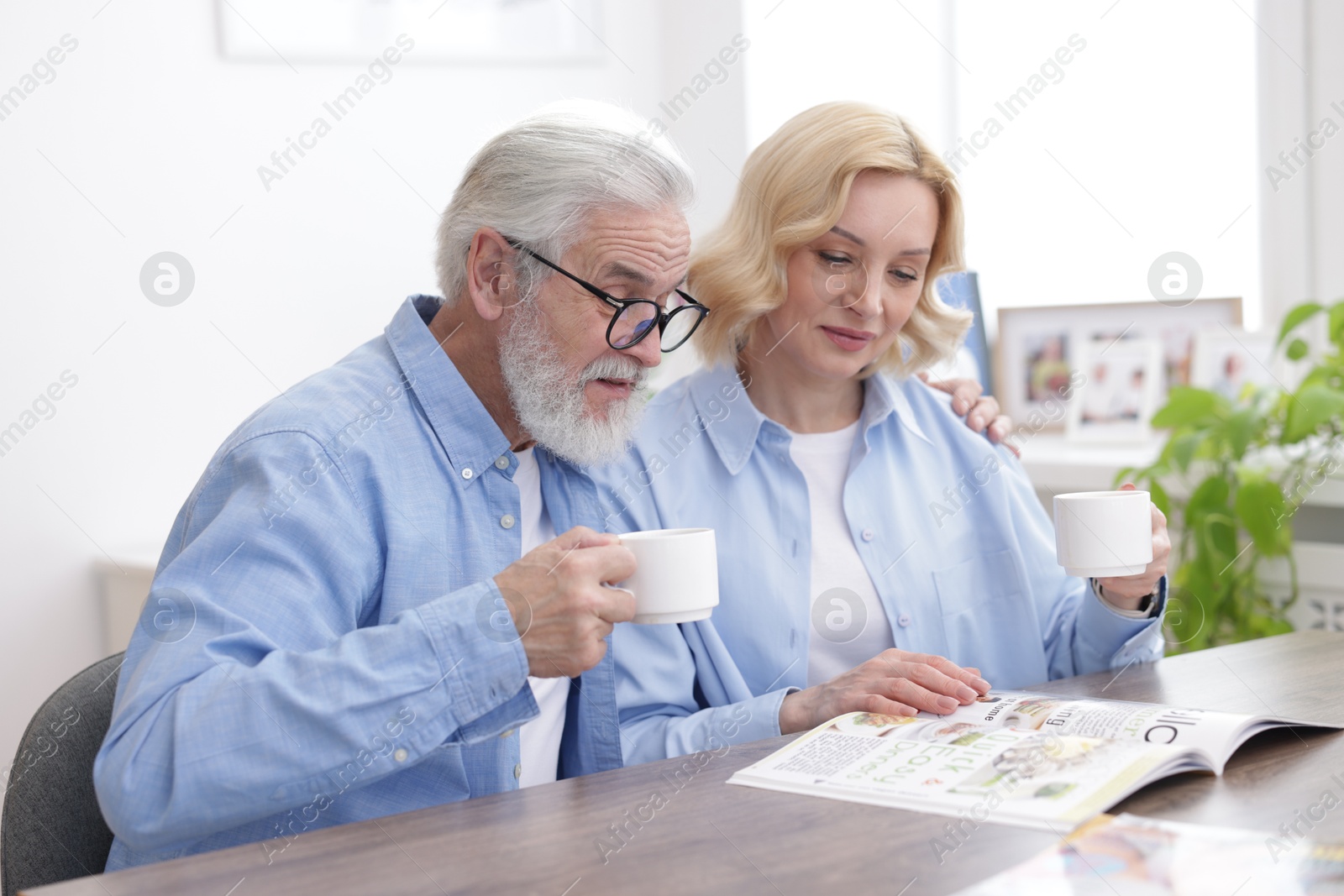 Photo of Senior man and mature woman with coffee reading magazine at home. Happy couple