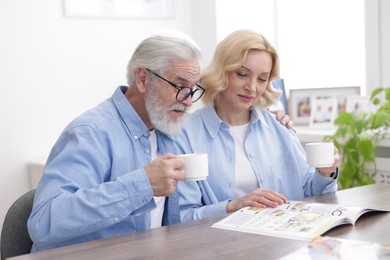 Senior man and mature woman with coffee reading magazine at home. Happy couple