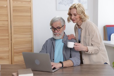 Senior man and mature woman watching something on laptop at home. Happy couple