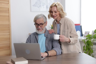 Photo of Senior man and mature woman watching something on laptop at home. Happy couple