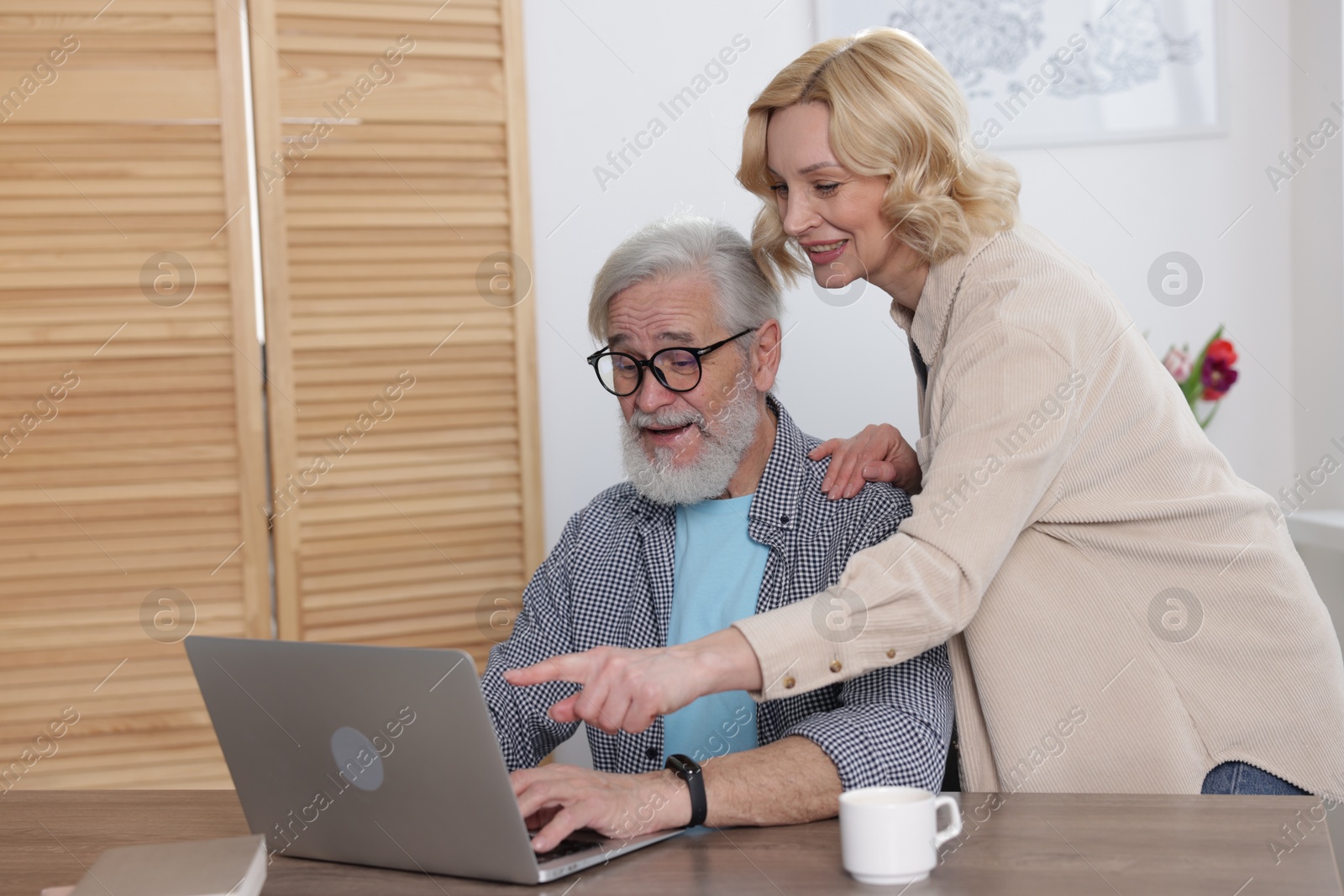 Photo of Senior man and mature woman watching something on laptop at home. Happy couple