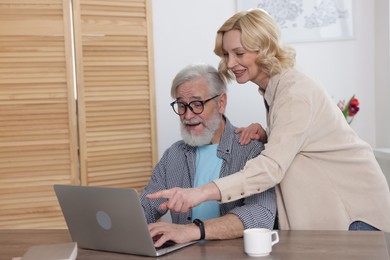 Senior man and mature woman watching something on laptop at home. Happy couple