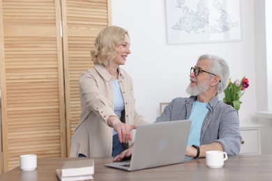 Photo of Senior man and mature woman with laptop at home. Happy couple