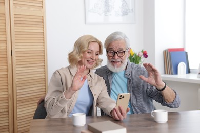 Photo of Senior man and mature woman having video chat via smartphone at home. Happy couple