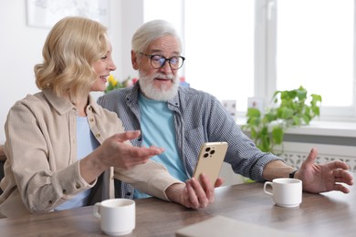 Photo of Senior man and mature woman watching something on smartphone at home. Happy couple