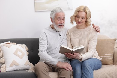 Senior man and mature woman reading book at home. Happy couple