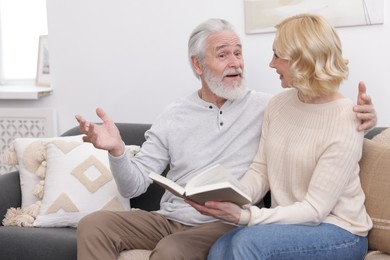 Senior man and mature woman with book spending time together at home. Happy couple