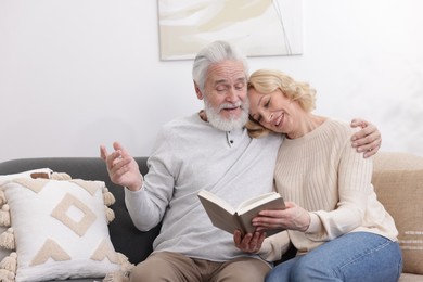 Senior man and mature woman reading book at home. Happy couple