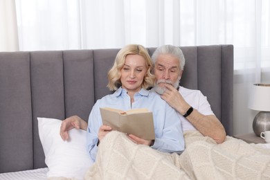 Senior man and mature woman reading book at home. Happy couple