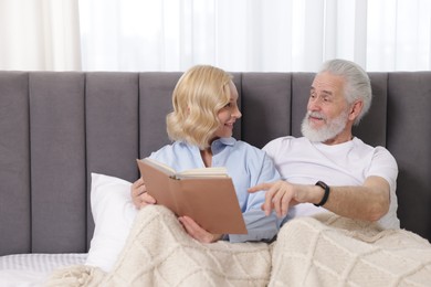 Senior man and mature woman with book spending time together at home. Happy couple