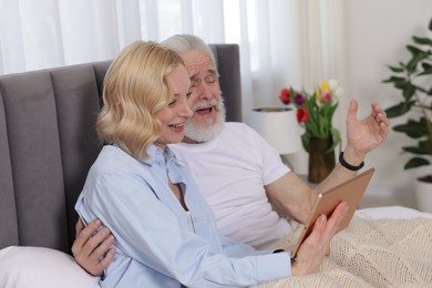 Photo of Senior man and mature woman watching something on tablet at home. Happy couple