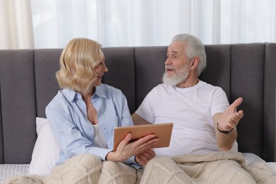 Senior man and mature woman with tablet spending time together at home. Happy couple