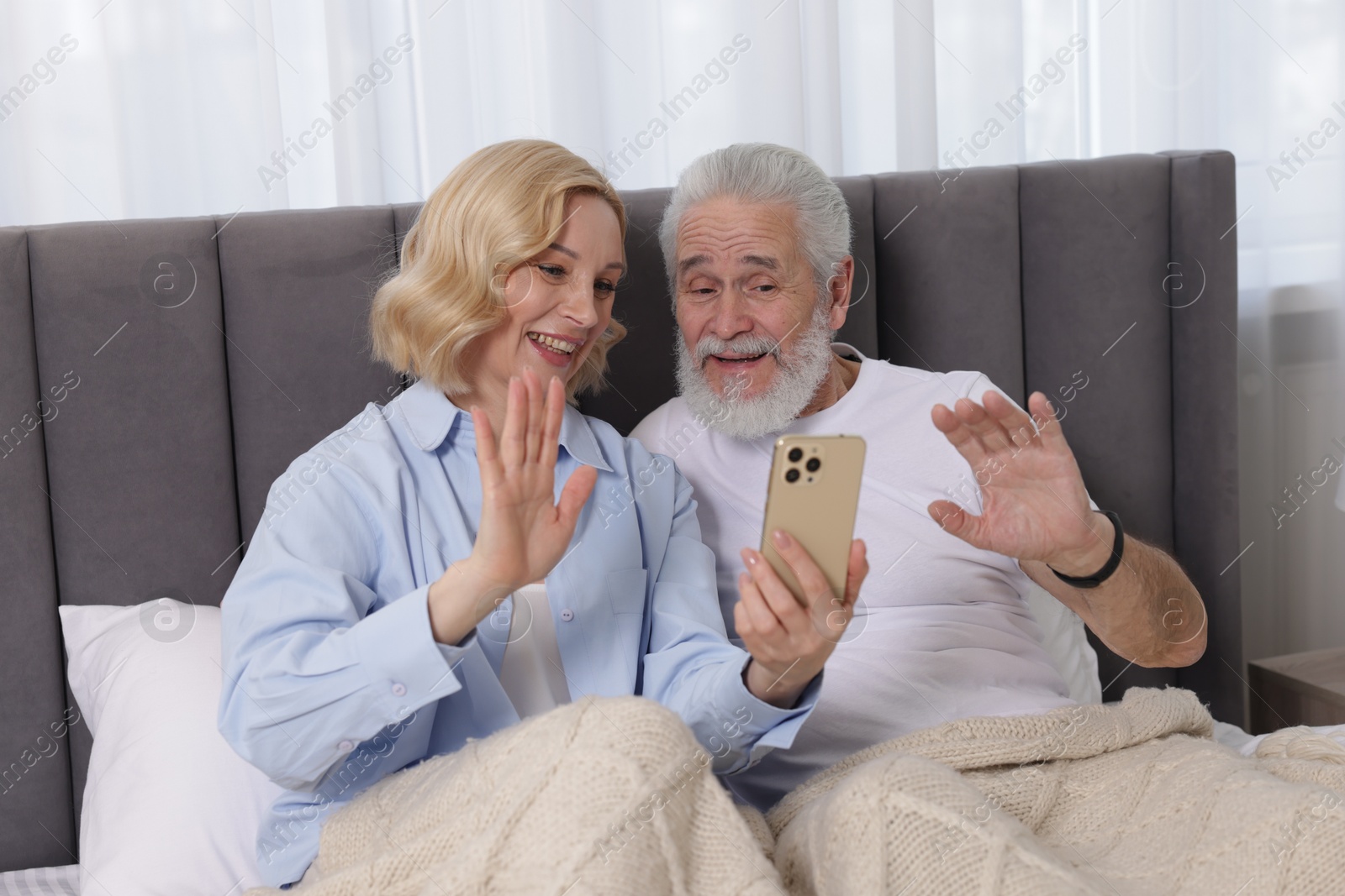 Photo of Senior man and mature woman having video chat via smartphone at home. Happy couple