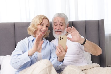 Photo of Senior man and mature woman having video chat via smartphone at home. Happy couple