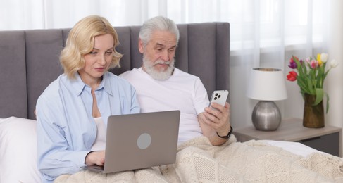 Senior man with smartphone and mature woman using laptop at home. Happy couple