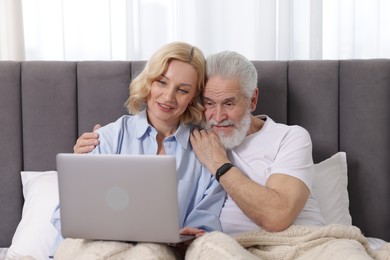 Photo of Senior man and mature woman watching something on laptop at home. Happy couple