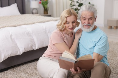 Senior man and mature woman reading book at home. Happy couple