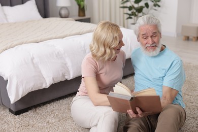 Senior man and mature woman reading book at home. Happy couple