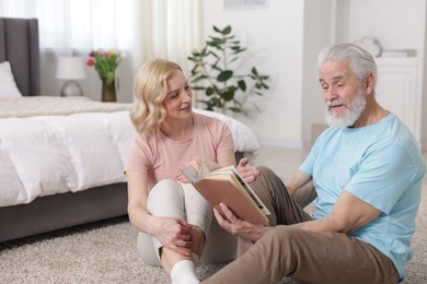 Senior man and mature woman reading book at home. Happy couple