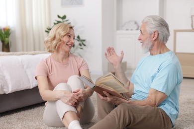 Senior man with book and mature woman spending time together at home. Happy couple