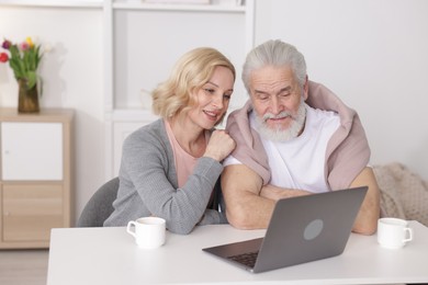 Photo of Senior man and mature woman watching something on laptop at home. Happy couple