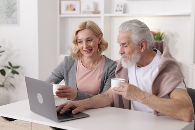 Senior man and mature woman watching something on laptop at home. Happy couple