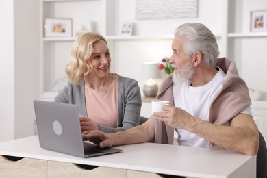 Photo of Senior man and mature woman with laptop spending time together at home. Happy couple