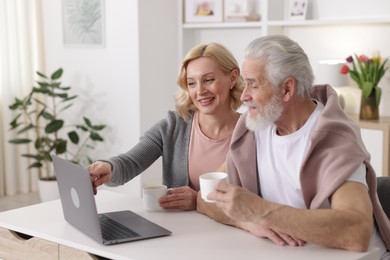 Photo of Senior man and mature woman watching something on laptop at home. Happy couple