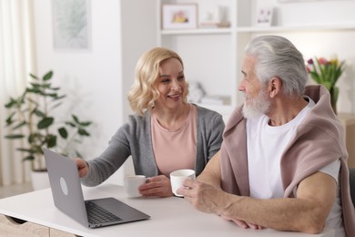 Senior man and mature woman with laptop spending time together at home. Happy couple