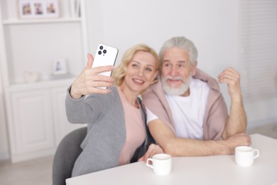 Photo of Senior man and mature woman taking selfie at home, selective focus. Happy couple