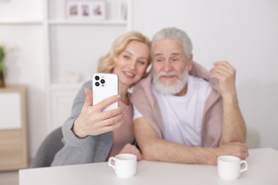 Senior man and mature woman taking selfie at home, selective focus. Happy couple