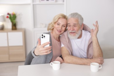 Senior man and mature woman taking selfie at home, selective focus. Happy couple