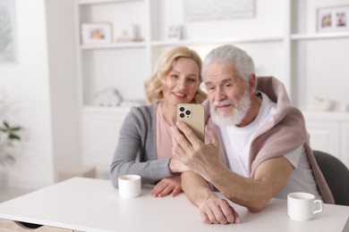 Photo of Senior man and mature woman watching something on smartphone at home, selective focus. Happy couple