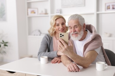 Photo of Senior man and mature woman watching something on smartphone at home, selective focus. Happy couple