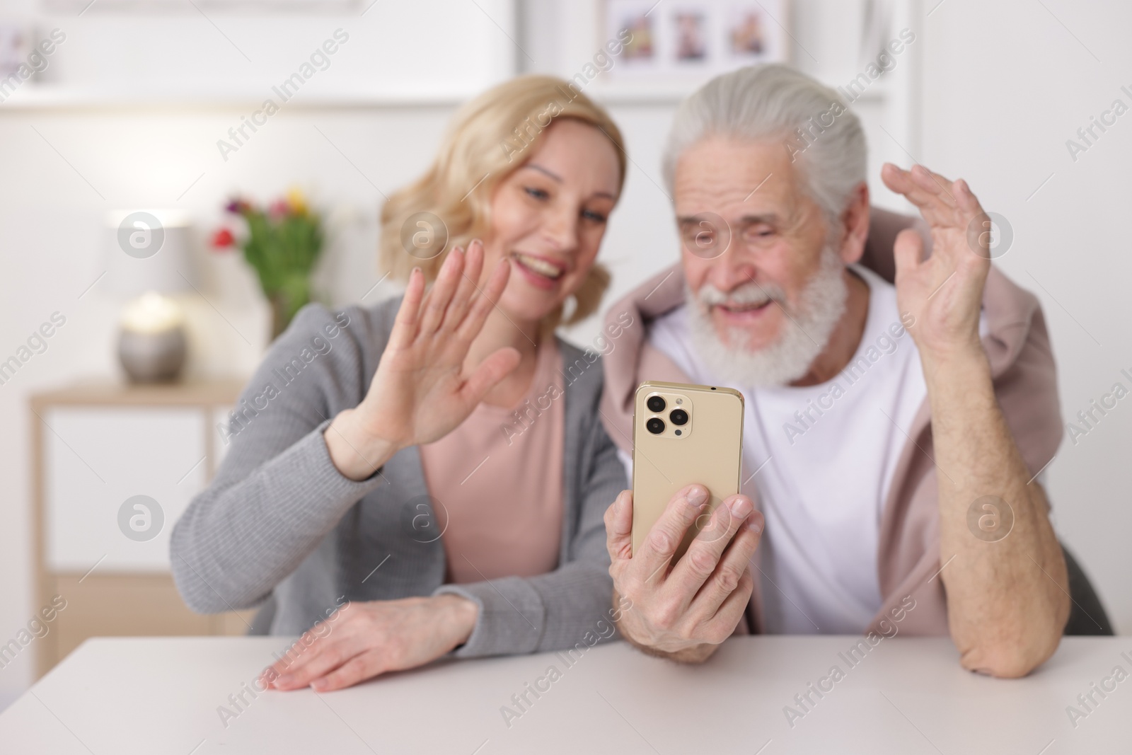 Photo of Senior man and mature woman having video chat via smartphone at home, selective focus. Happy couple