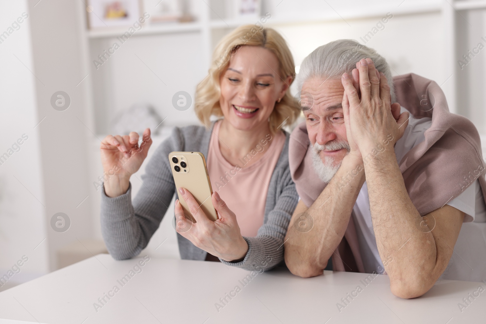 Photo of Senior man and mature woman watching something on smartphone at home, selective focus. Happy couple