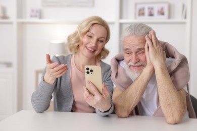 Photo of Senior man and mature woman watching something on smartphone at home, selective focus. Happy couple