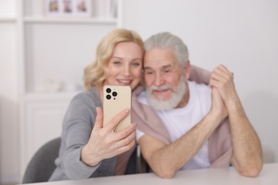 Senior man and mature woman watching something on smartphone at home, selective focus. Happy couple