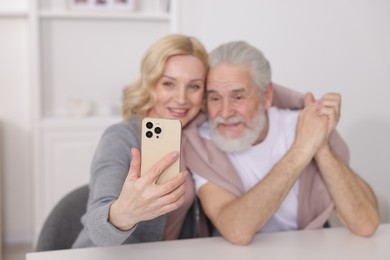 Senior man and mature woman watching something on smartphone at home, selective focus. Happy couple