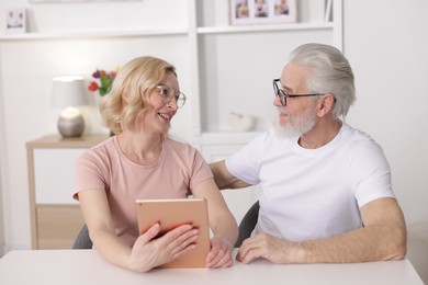 Senior man and mature woman with tablet spending time together at home. Happy couple